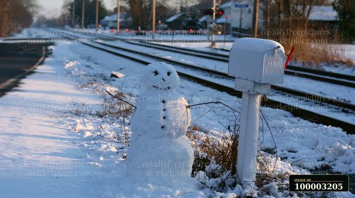 A snowman beside a snow-covered mailbox stands near a railroad track.