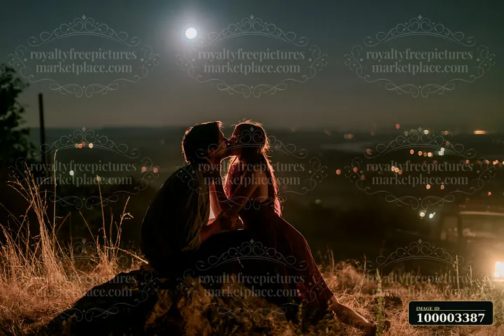 Lovers kissing on a mountain overlook at night, surrounded by a beautiful view of twinkling city lights under a bright moon.