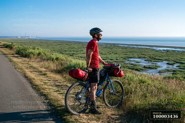 A person stands next to a bicycle, looking out over a coastline with salt marsh.