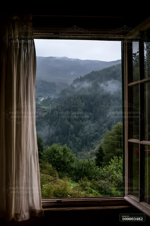 Raindrops slide down a cabin window, revealing a mountain landscape with lush greenery and mist rolling over the hills.
