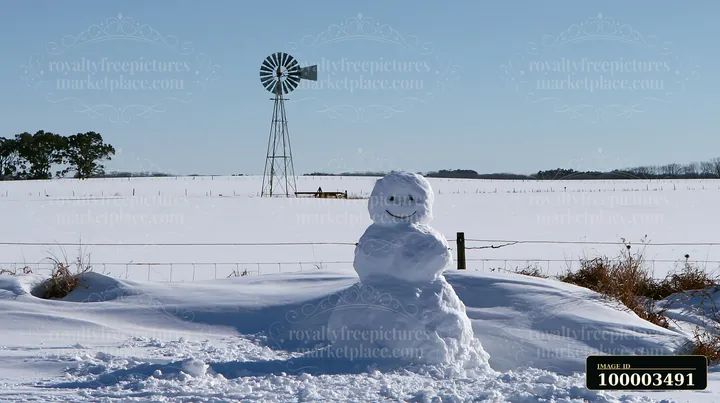 A snowman surrounded by snowdrifts stands in a winter landscape with a windmill in the background.