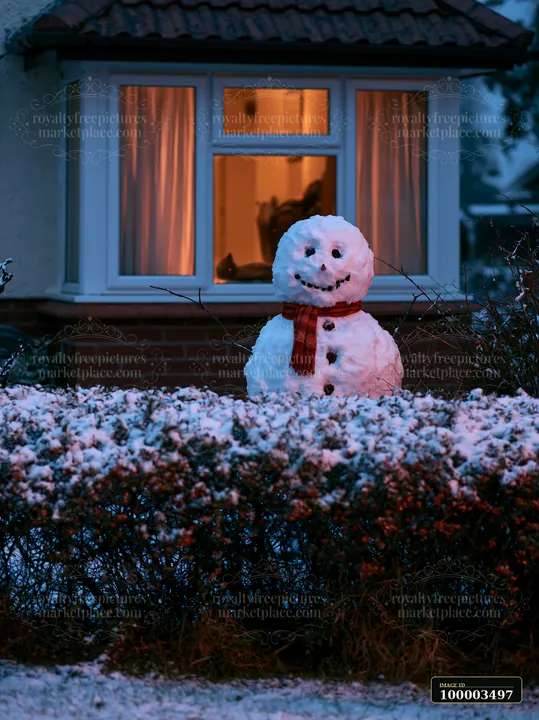 A snowman stands outside a cottage window during dusk.
