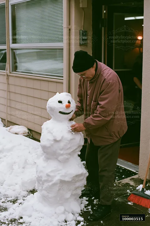 An adult shaping a snowman in front of a house during winter.