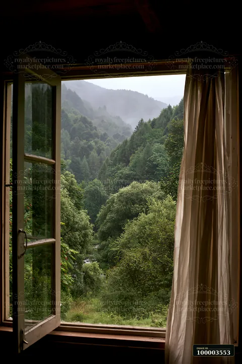 Raindrops fall on a cabin window, revealing a mountain landscape with dense green trees and mist covering the hills.