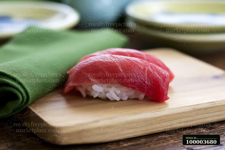 A single tuna nigiri is placed on a wooden board next to a green napkin.