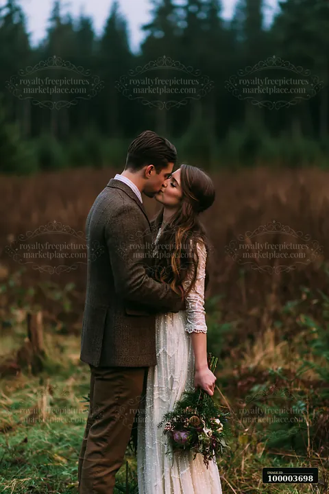 Bride and groom kiss while embracing in a forest, with the bride holding a floral bouquet.