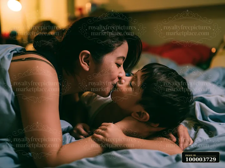 Parent and child share a tender kiss in bed at bedtime under warm indoor light.