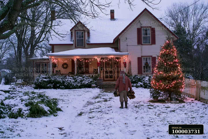 A snowy country house features Christmas lights and a person walking towards it while carrying wood.