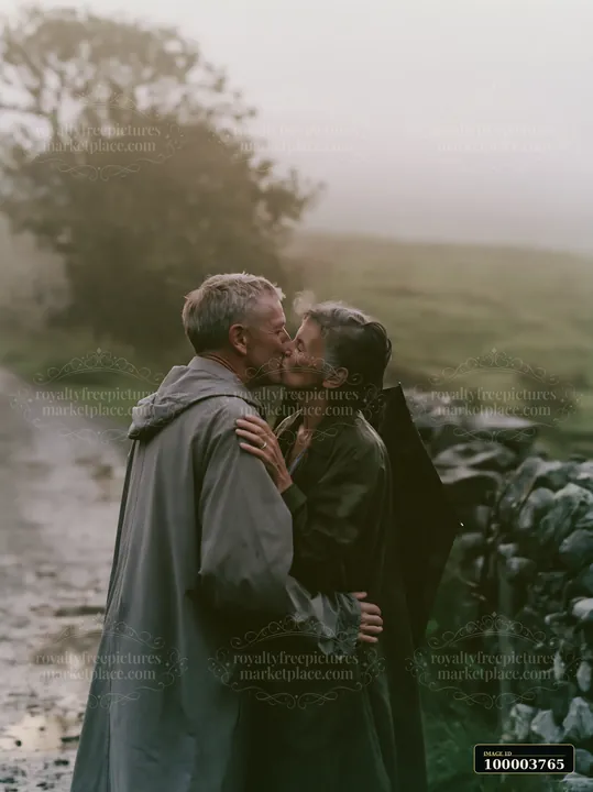A couple kisses on a country road surrounded by green fields and stone walls.