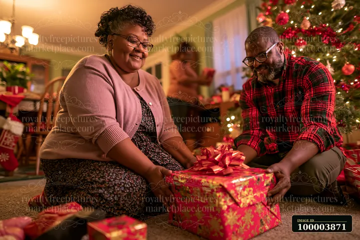 Two parents arrange wrapped gifts beside a decorated Christmas tree in a warmly lit living room.