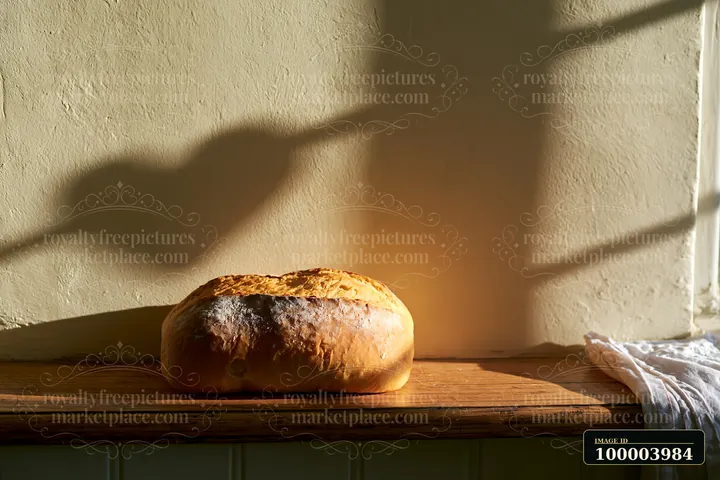 Rustic loaf of bread on a wooden surface with warm window light and a heart-shaped shadow on the wall.
