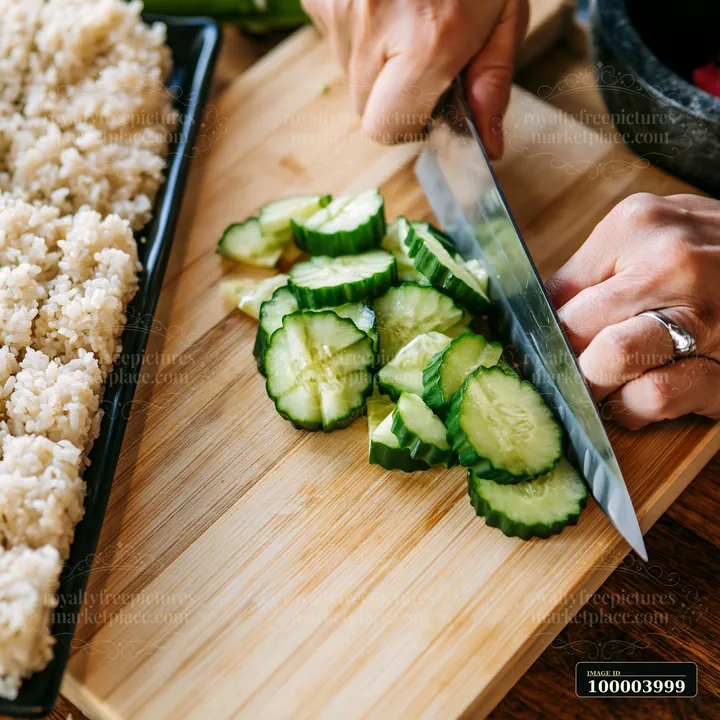 A sushi chef is cutting cucumbers into slices on a wooden cutting board.
