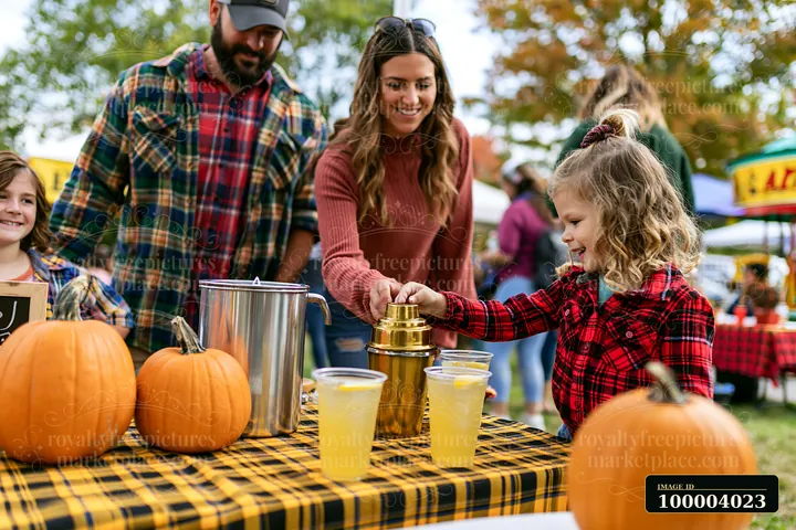 A family shares lemonade at an outdoor festival near pumpkins.