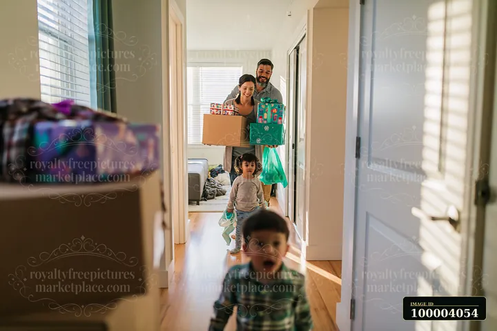 Parents carry decorated gift boxes while walking through their home.