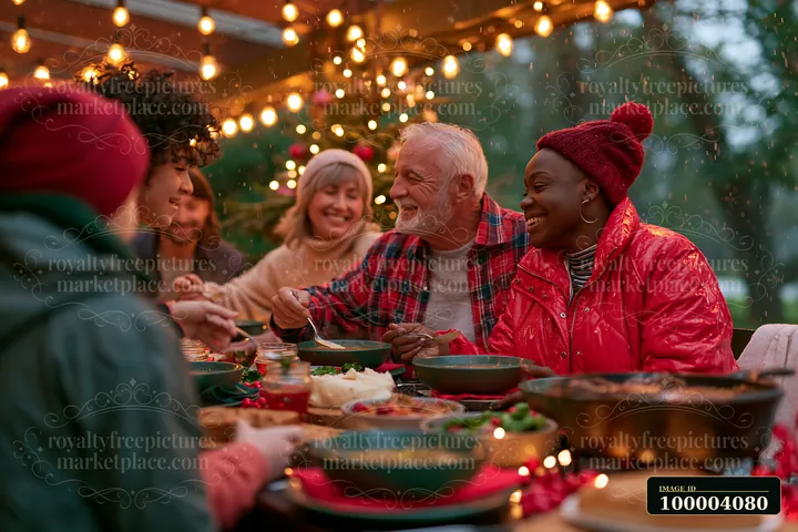 Several generations share a festive Christmas meal outdoors beneath glowing string lights as light snow falls.