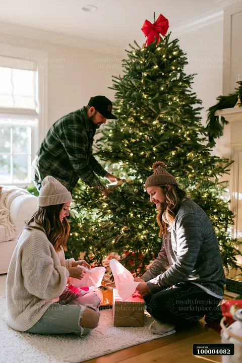A couple prepares for Christmas by placing gifts under a decorated tree in their living room.