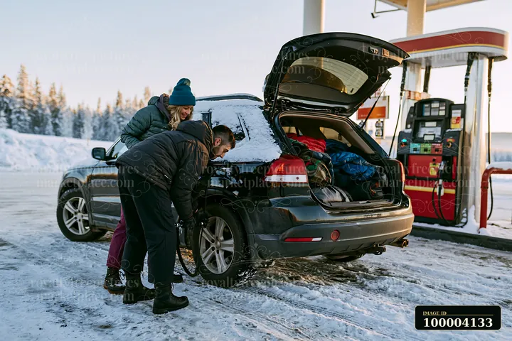A couple checks the car's tire at a gas station before a winter holiday road trip.