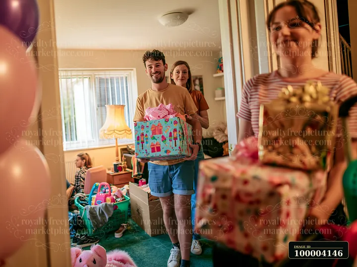 A man and woman carry decorated gift boxes into a room filled with children.