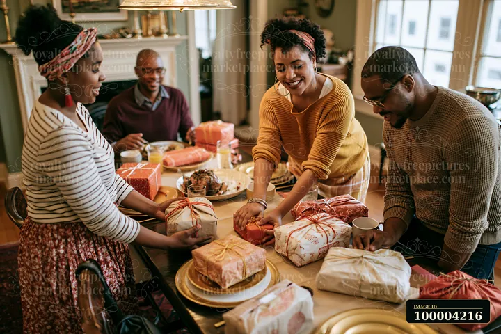 Family members work together to place wrapped gifts on a dining table filled with food and decorations.