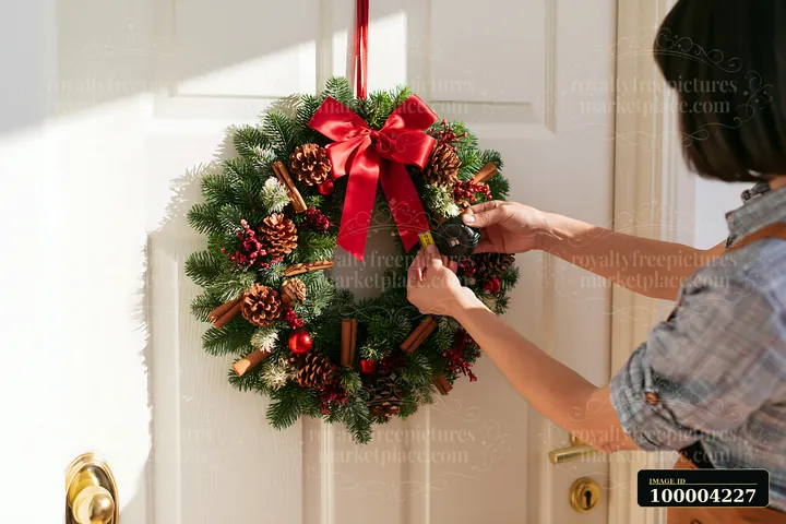 Person hangs a decorated Christmas wreath on a bright apartment door.