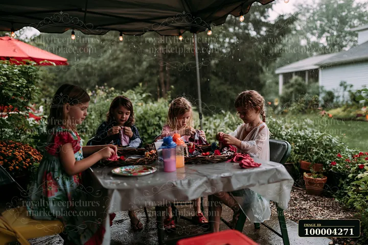 Four children sit at a table in a backyard, crafting handmade ornaments.