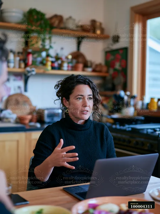 Businesswoman gestures while speaking beside an open laptop at a cafe table.