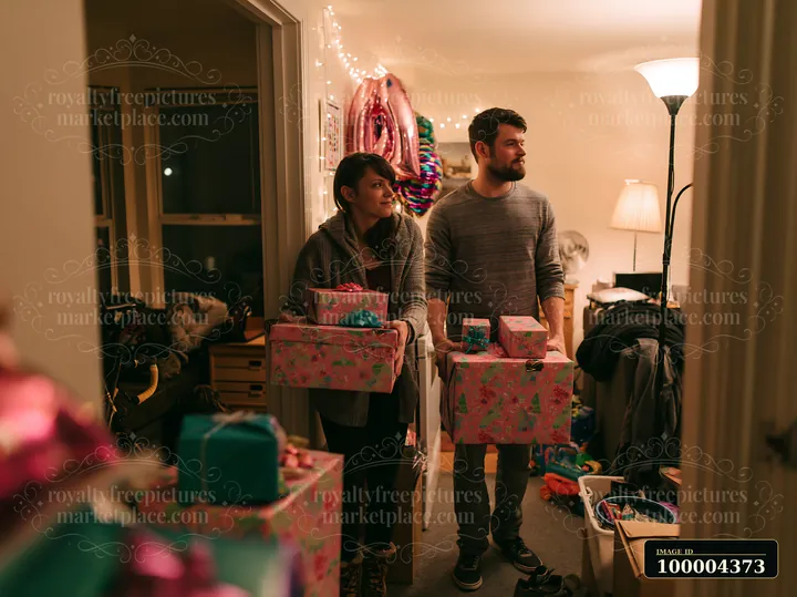 Two parents carry decorated gift boxes through a warmly lit home with festive decorations.
