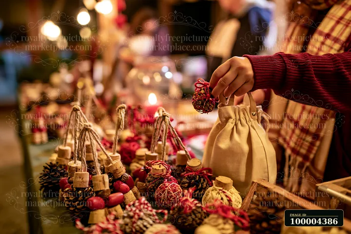 Shopper holds a handmade ornament and fabric gift bag at a warmly lit Christmas market stall.