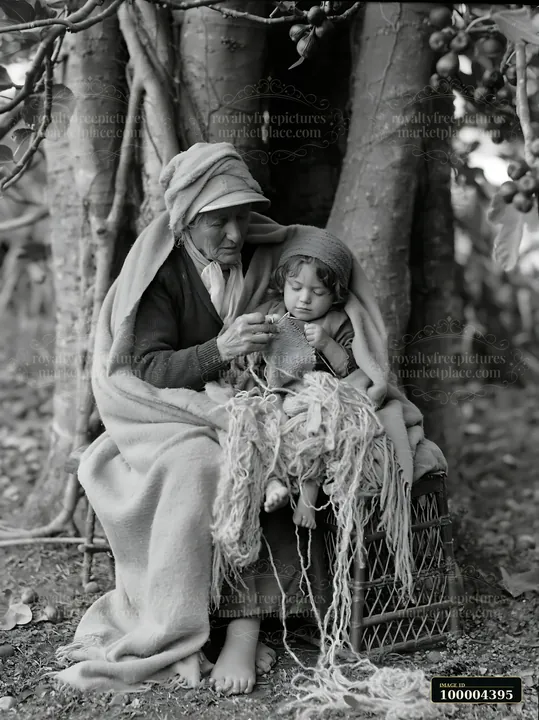 An elder and a child sit together covered in warm blankets beneath a tree.