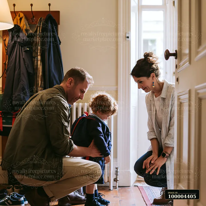 Parents comfort a young child wearing a backpack in a warmly lit home entryway before school.