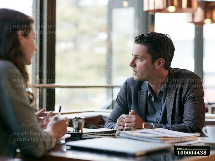 Businessman discusses paperwork with a female advisor across a table in a bright meeting space.