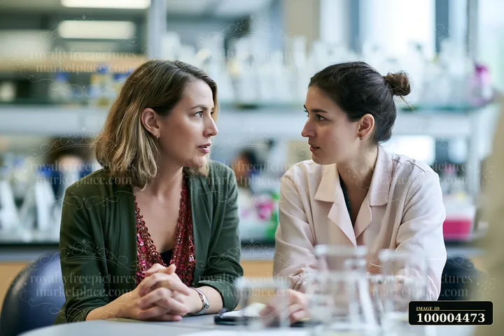 A businesswoman engages in a coaching session with an employee in a lab setting.