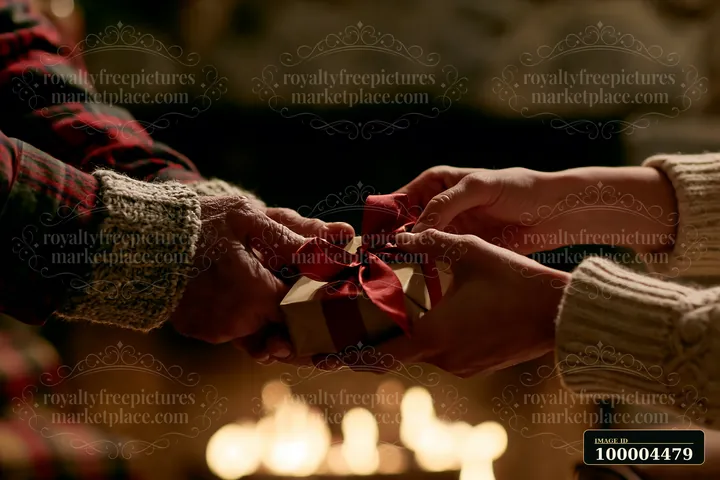 Two pairs of hands exchange a wrapped gift with a red ribbon in warm candlelight.