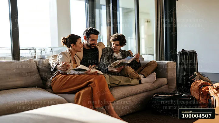 White family reads together on a sofa in a bright modern living room with luggage nearby.