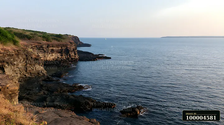 A coastal cliff rises above blue waters with rocky shores below.