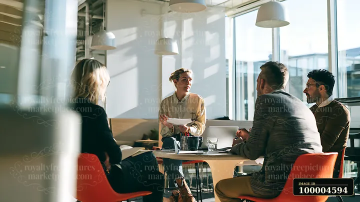 Businesswoman presents documents to three colleagues around a table in a bright shared coworking office.
