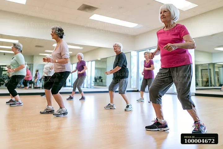 Senior women practice dance fitness together in a bright mirrored studio with polished wood floors.